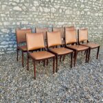 Lot de 8 chaises Johannes Andersen en palissandre massif et cuir noir, vues de trois-quarts dans un décor lumineux.