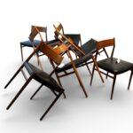 Photographie d'une suite de huit chaises vintage de salle à manger de style scandinave, attribuées au designer Arne Vodder. Les chaises sont alignées sur deux rangées sur un parquet en bois clair. Elles présentent une structure en bois massif aux tons chauds et une assise revêtue de cuir noir en excellent état. L'arrière-plan montre un mur blanc avec des fenêtres aux boiseries en bois et une prise électrique.